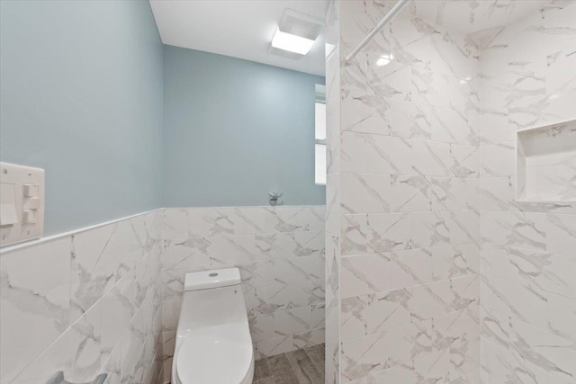 bathroom with a marble finish shower, a wainscoted wall, tile walls, and toilet