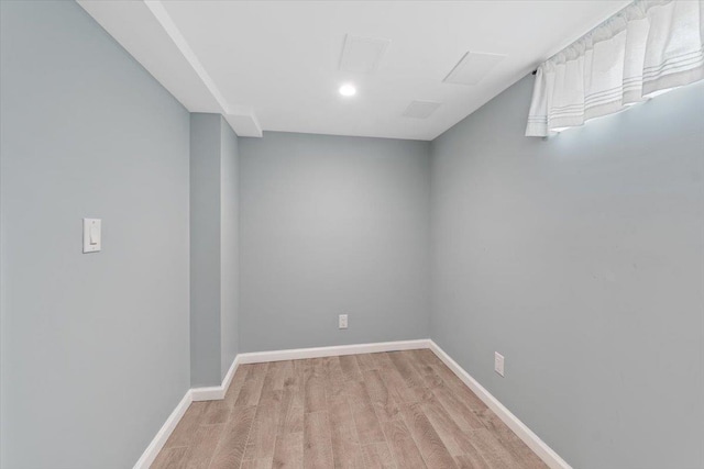 spare room featuring attic access, light wood-style floors, and baseboards