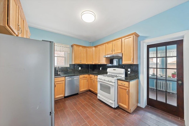 kitchen featuring stainless steel appliances, dark stone countertops, backsplash, and under cabinet range hood