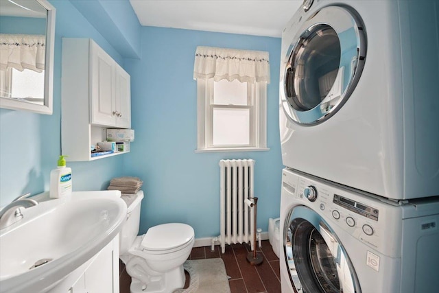 laundry room featuring radiator heating unit, wood tiled floor, a sink, stacked washing maching and dryer, and laundry area