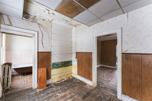 empty room featuring a drop ceiling, dark hardwood / wood-style flooring, and wood walls