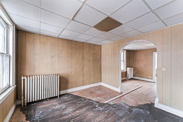 unfurnished room featuring wooden walls, radiator, and a drop ceiling