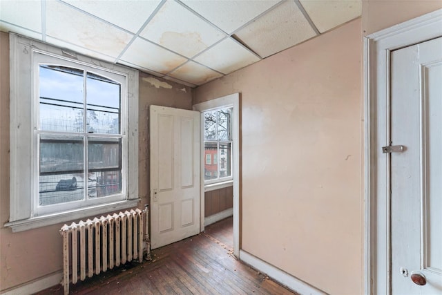 empty room with a drop ceiling, dark hardwood / wood-style flooring, and radiator heating unit