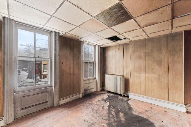 empty room with radiator, a paneled ceiling, and wooden walls