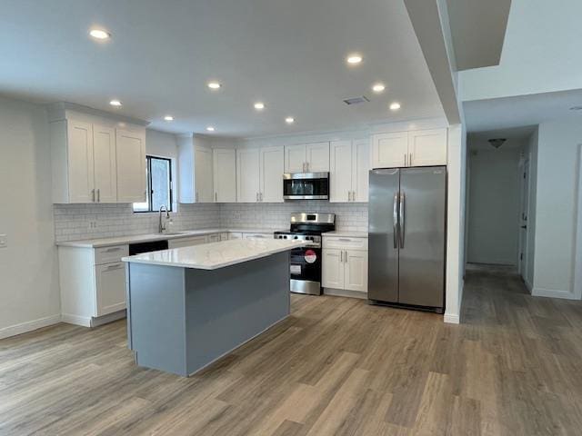 kitchen featuring stainless steel appliances, light countertops, a center island, and white cabinetry