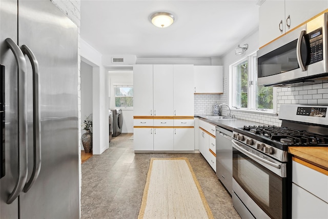 kitchen featuring sink, washing machine and clothes dryer, white cabinetry, stainless steel appliances, and decorative backsplash