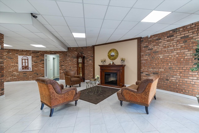 living area featuring brick wall, a glass covered fireplace, and a paneled ceiling