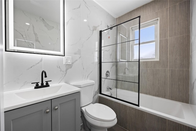 full bathroom with tile walls, shower / bath combination with glass door, vanity, and toilet
