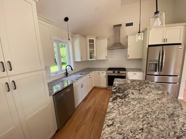 kitchen featuring pendant lighting, sink, wall chimney range hood, white cabinetry, and stainless steel appliances