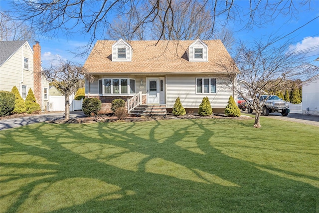 new england style home featuring fence, a front yard, and a shingled roof