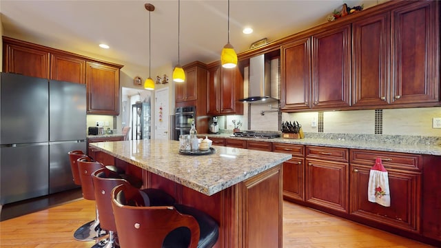 kitchen with appliances with stainless steel finishes, light wood-style flooring, wall chimney range hood, and light stone counters