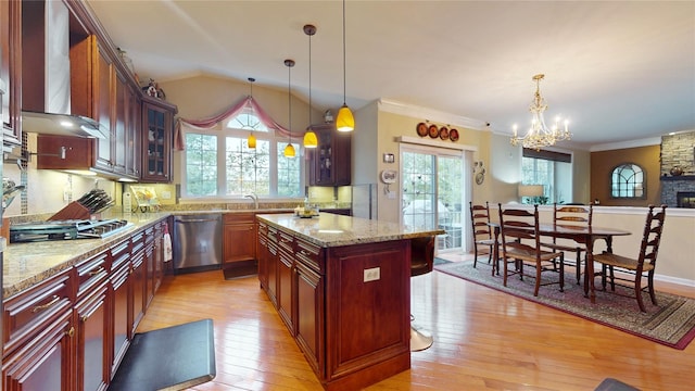 kitchen with stainless steel appliances, wall chimney range hood, light wood-style flooring, and decorative light fixtures