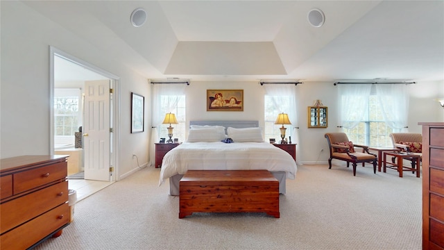 bedroom with a tray ceiling, light colored carpet, and multiple windows