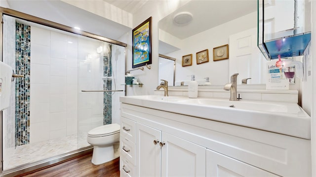 bathroom featuring double vanity, toilet, a stall shower, a sink, and wood finished floors