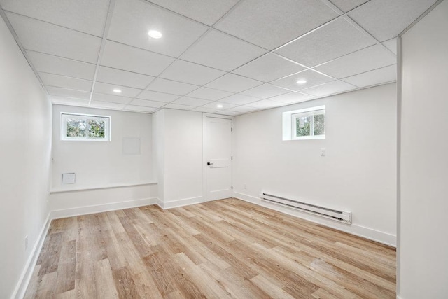 basement featuring a baseboard radiator, baseboards, a paneled ceiling, and light wood finished floors