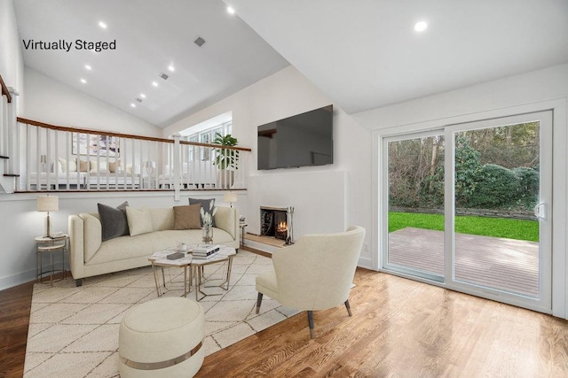 living area featuring a healthy amount of sunlight, a warm lit fireplace, wood finished floors, and recessed lighting