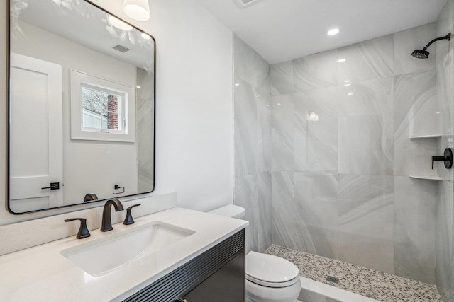 bathroom featuring visible vents, toilet, a tile shower, vanity, and recessed lighting