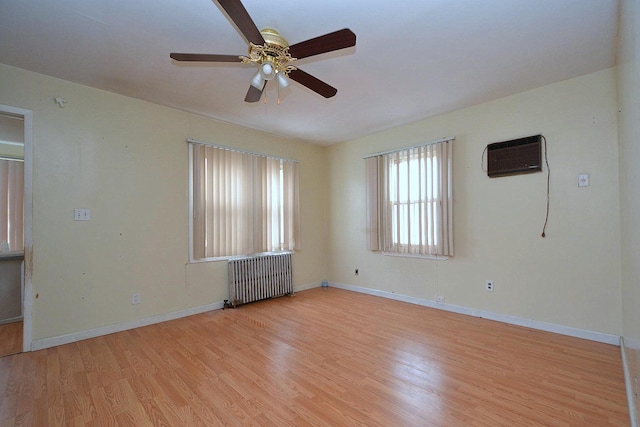 unfurnished room featuring baseboards, radiator heating unit, a wall unit AC, and light wood-style floors