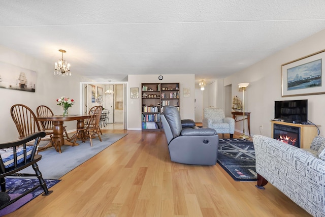 living area with a textured ceiling, a chandelier, wood finished floors, and a glass covered fireplace