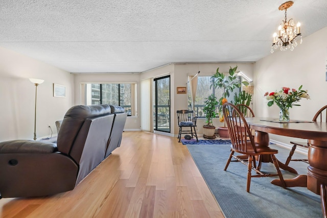 living room featuring a textured ceiling, light wood finished floors, a chandelier, and baseboards