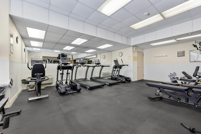 exercise room featuring a paneled ceiling and baseboards