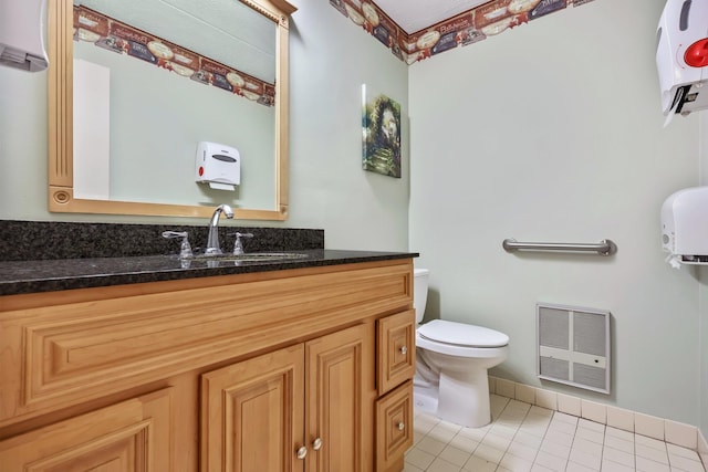 half bathroom featuring heating unit, toilet, vanity, baseboards, and tile patterned floors