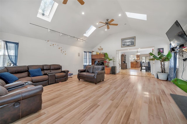 living room with ceiling fan with notable chandelier, light hardwood / wood-style flooring, high vaulted ceiling, and a skylight