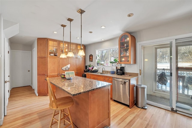 kitchen featuring dark stone countertops, light hardwood / wood-style flooring, a center island, dishwasher, and hanging light fixtures