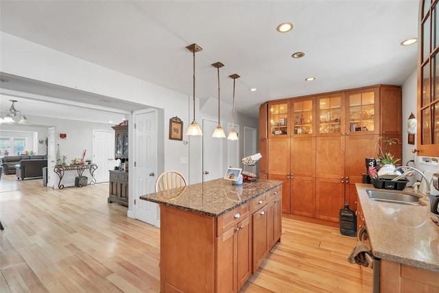 kitchen with light hardwood / wood-style flooring, hanging light fixtures, dark stone counters, a center island, and sink