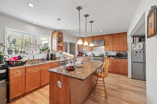 kitchen with sink, pendant lighting, a kitchen island, stainless steel appliances, and wall chimney exhaust hood