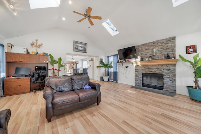 living room featuring high vaulted ceiling, light hardwood / wood-style flooring, a stone fireplace, ceiling fan, and a skylight