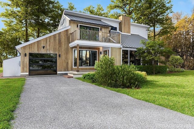 view of front facade with a standing seam roof, a balcony, a garage, driveway, and a front lawn