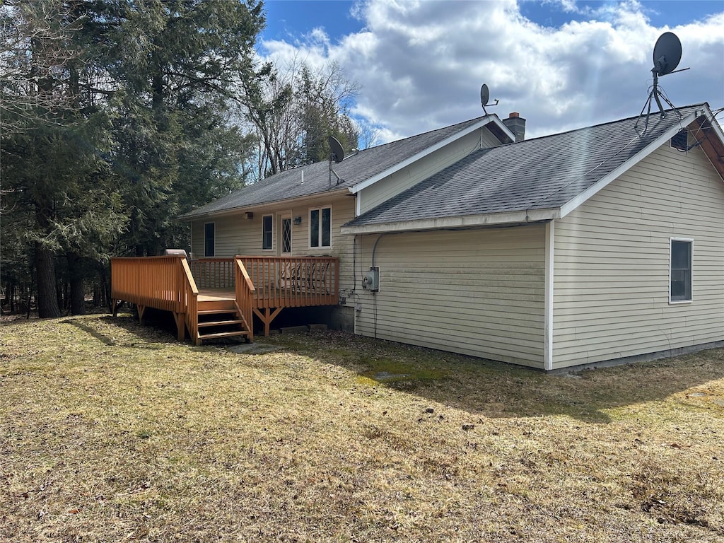back of house with a lawn, a deck, and roof with shingles