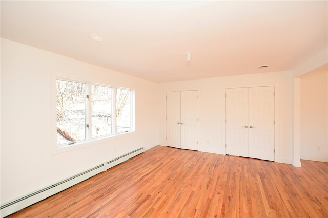 unfurnished bedroom featuring multiple closets, baseboard heating, and light hardwood / wood-style flooring