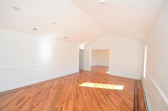 empty room featuring vaulted ceiling, light wood-type flooring, and a baseboard heating unit