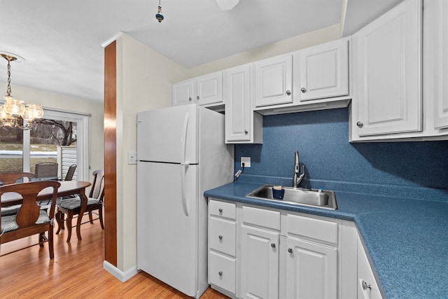 kitchen with light wood finished floors, white cabinets, a sink, and freestanding refrigerator