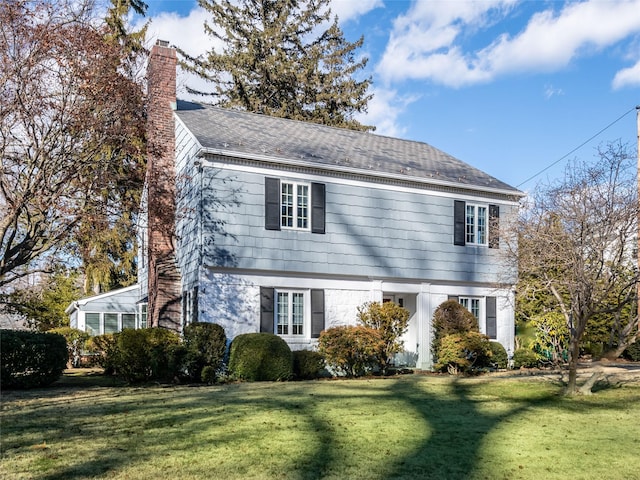 colonial-style house featuring a chimney and a front lawn