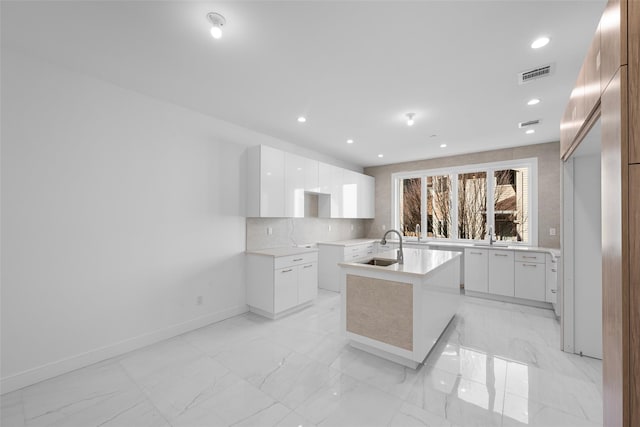 kitchen featuring white cabinetry, sink, backsplash, and a center island with sink