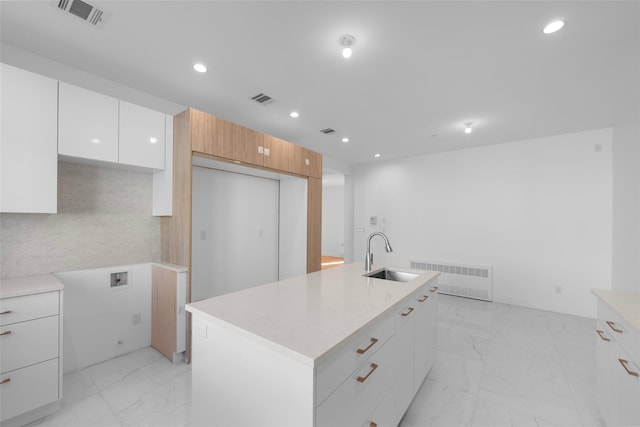 kitchen featuring radiator, white cabinetry, sink, decorative backsplash, and a kitchen island with sink