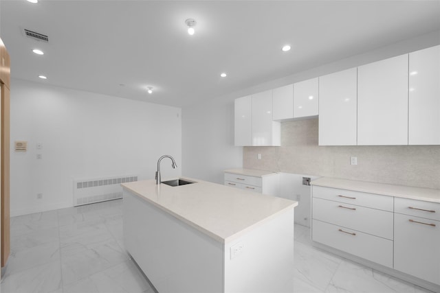 kitchen with sink, radiator, an island with sink, decorative backsplash, and white cabinets