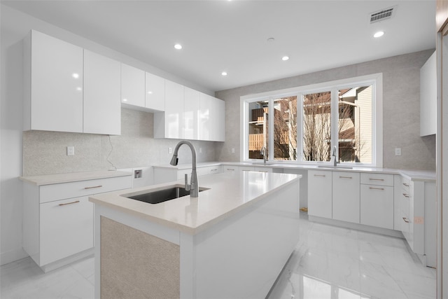 kitchen with a kitchen island with sink, sink, white cabinets, and backsplash