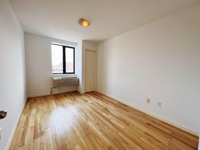 empty room featuring light wood-type flooring, a wall unit AC, and baseboards