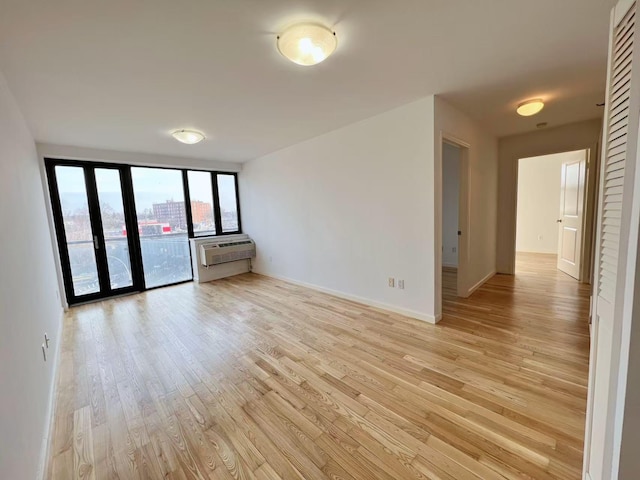 spare room featuring baseboards, light wood finished floors, and a wall mounted AC