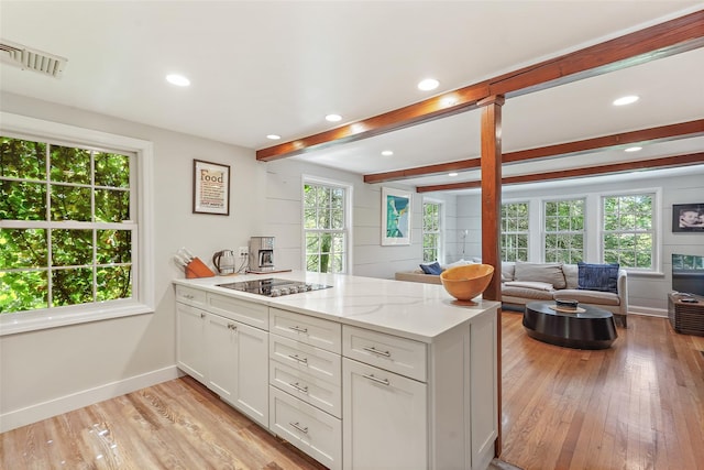 kitchen featuring light stone counters, beamed ceiling, light hardwood / wood-style floors, white cabinets, and black electric cooktop