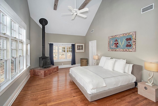 bedroom with ceiling fan, a wood stove, high vaulted ceiling, and light hardwood / wood-style floors