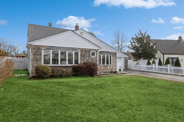 rear view of house featuring fence private yard, a shingled roof, a chimney, and a yard