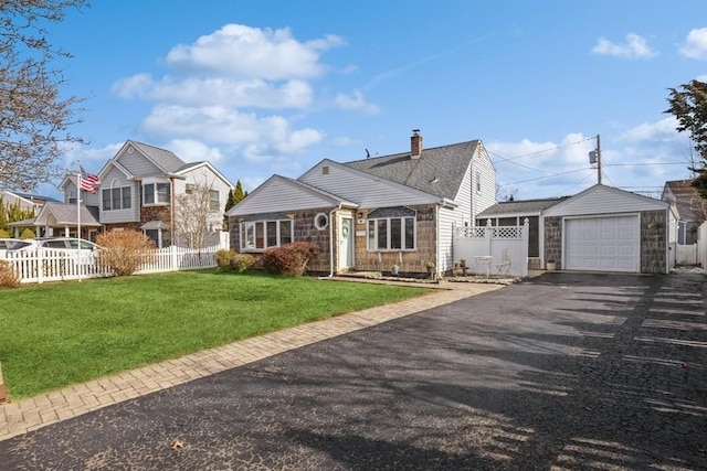 view of front of home with driveway, an outbuilding, an attached garage, fence, and a front lawn