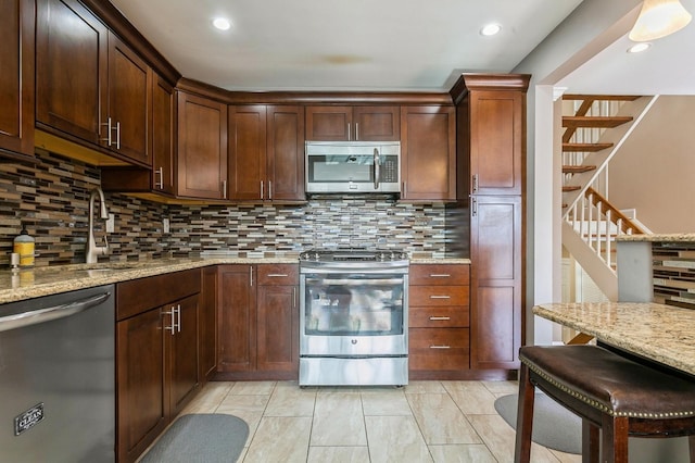 kitchen with decorative backsplash, appliances with stainless steel finishes, light stone countertops, a kitchen bar, and recessed lighting