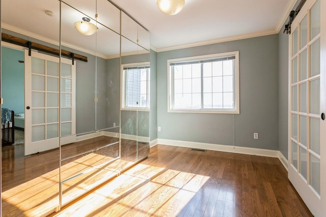 empty room featuring ornamental molding, a barn door, wood finished floors, and baseboards