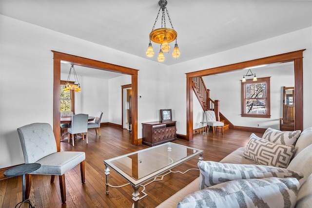 living area with an inviting chandelier, baseboards, stairway, and dark wood-style flooring